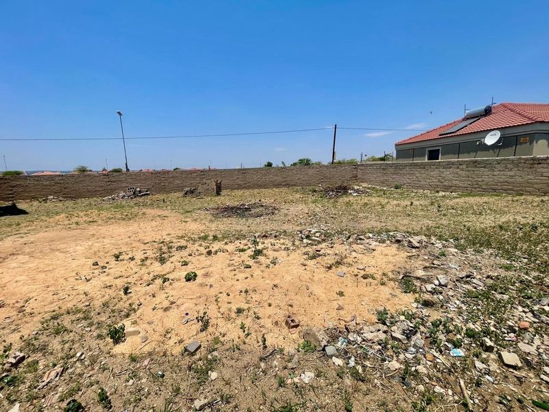 A vacant residential plot featuring a perimeter boundary wall and natural ground cover, suitable for future development.