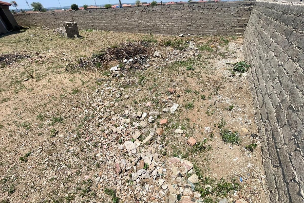 A vacant residential plot featuring a perimeter brick wall with electric fencing, currently requiring site clearing and landscaping.