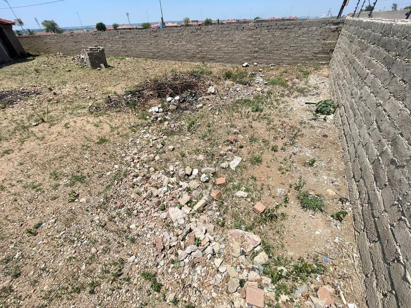 A vacant residential plot featuring a perimeter brick wall with electric fencing, currently requiring site clearing and landscaping.
