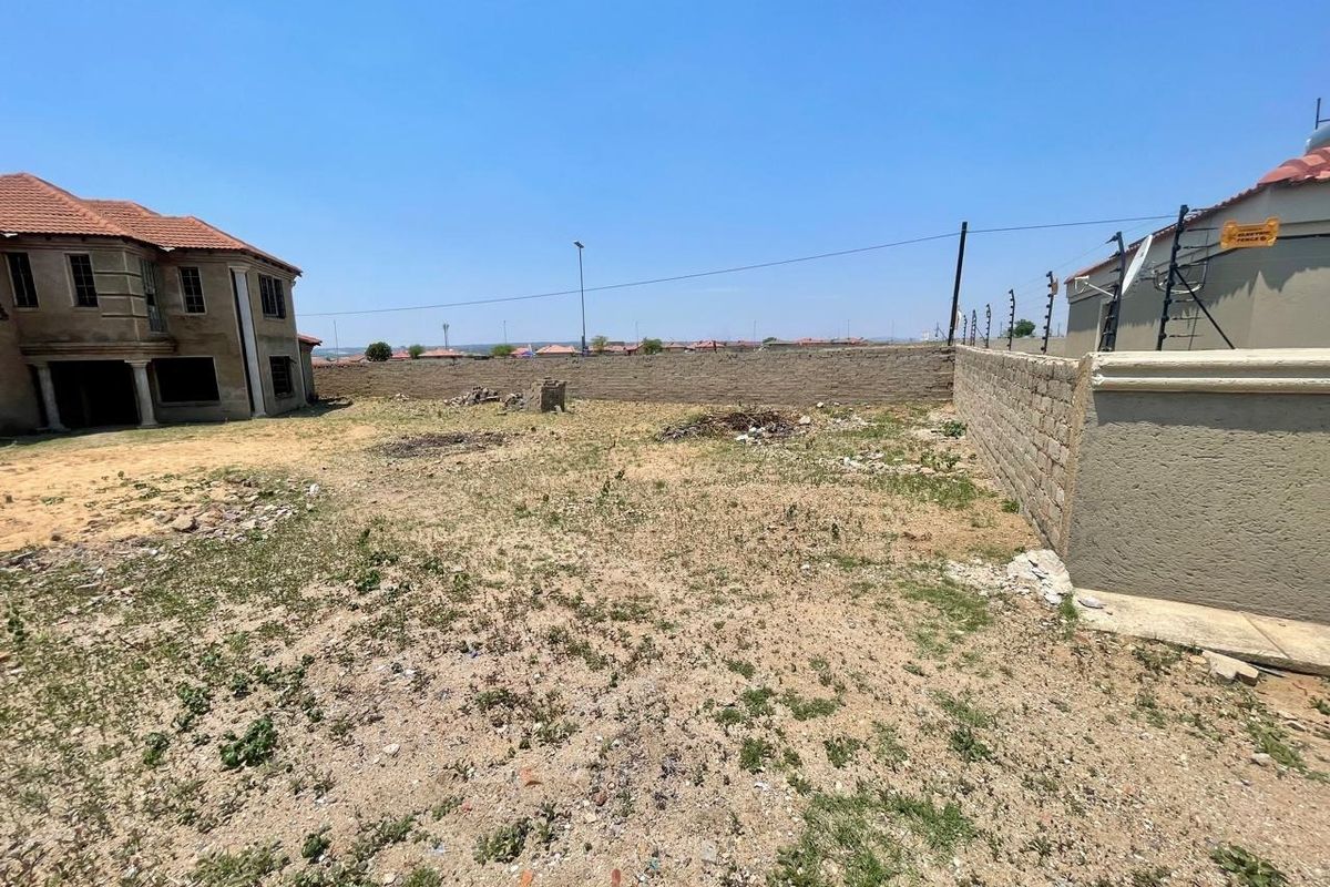 A vacant residential plot featuring perimeter walling and electric fencing, situated adjacent to existing residential structures.