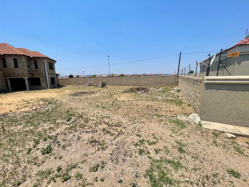 A vacant residential plot featuring perimeter walling and electric fencing, situated adjacent to existing residential structures.
