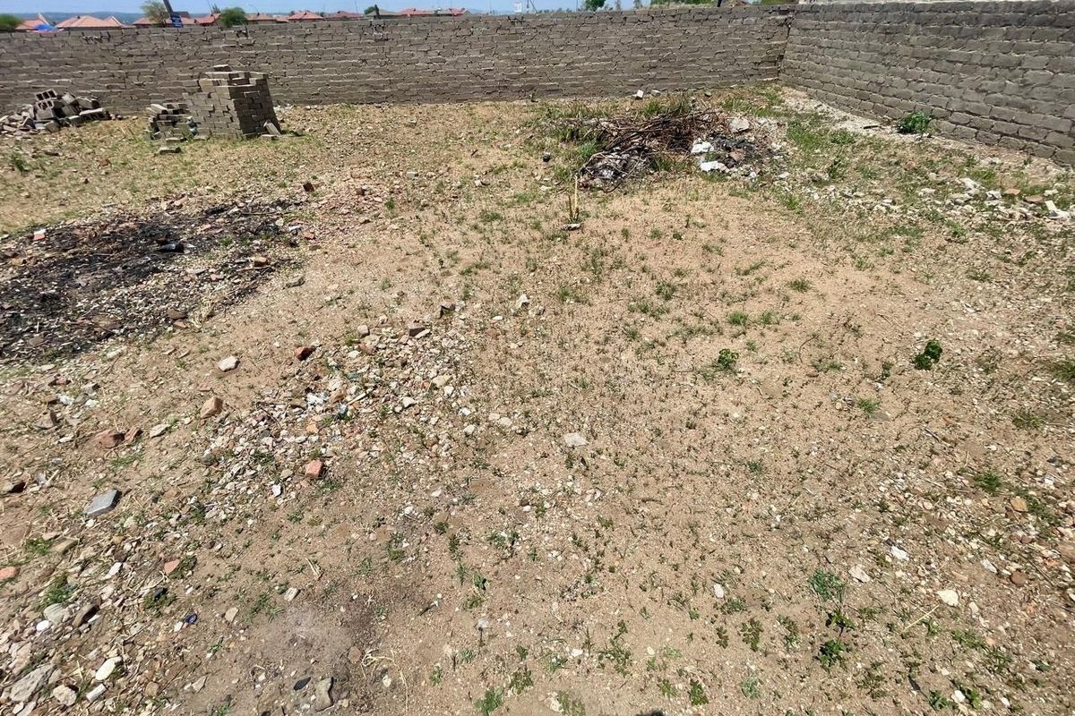 A vacant residential plot featuring a perimeter brick wall with electric fencing, currently requiring site clearing and landscaping.