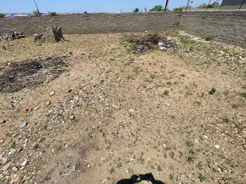 A vacant residential plot featuring a perimeter brick wall with electric fencing, currently requiring site clearing and landscaping.