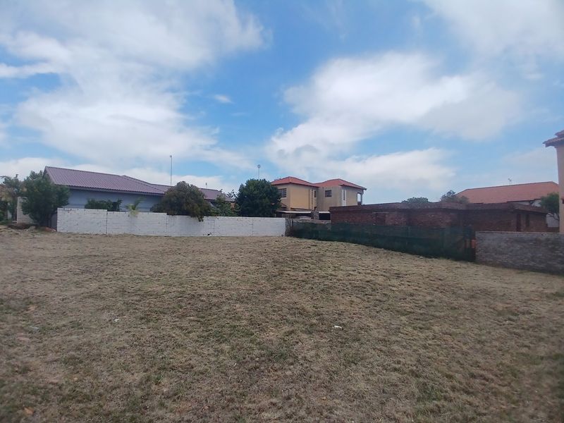 A vacant residential plot featuring a level grassed area enclosed by boundary walls and perimeter fencing, situated in a developed neighborhood.
