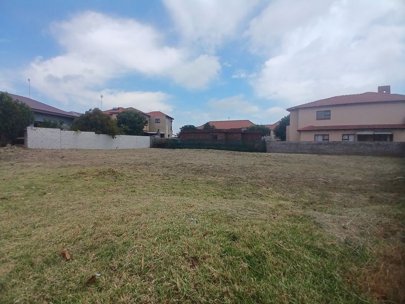 A vacant residential plot featuring a grass lawn and established perimeter boundary walls, situated within a developed neighborhood.