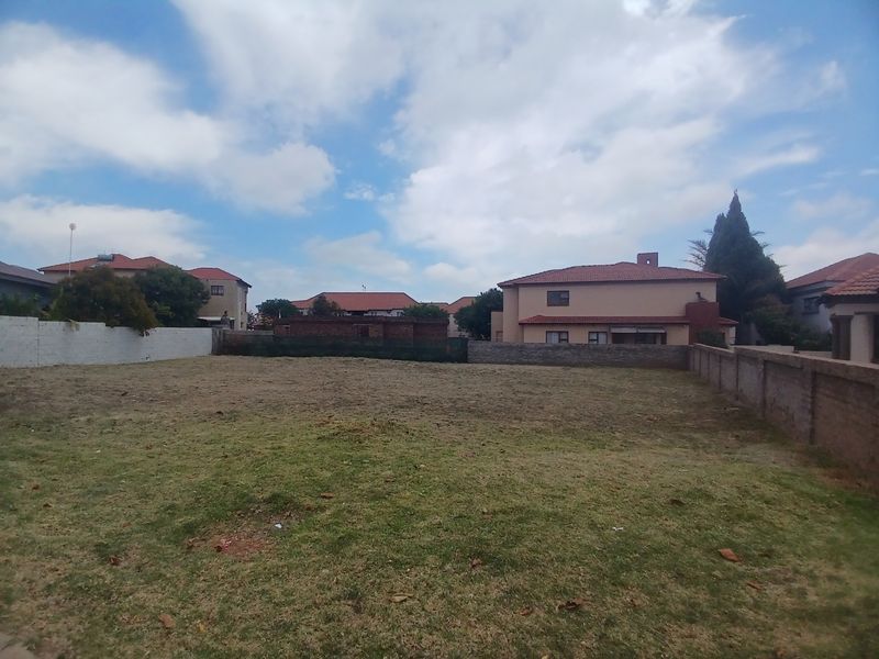 A vacant residential plot featuring a grass lawn enclosed by perimeter brick walls, situated within an established neighborhood.