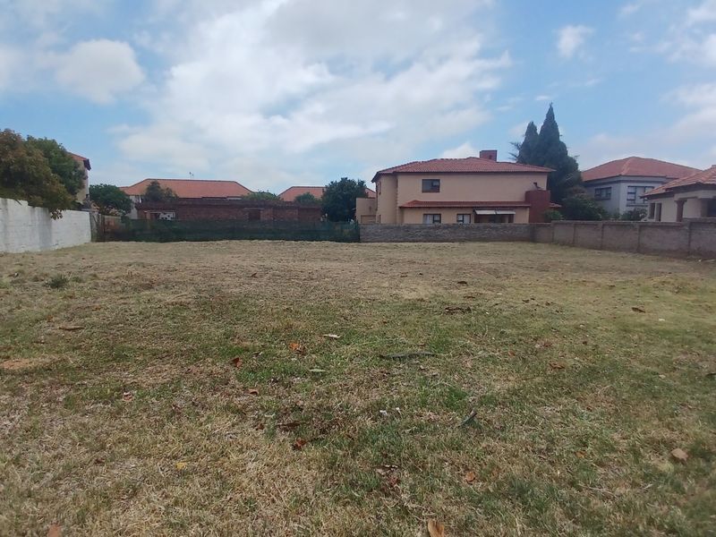 A vacant residential plot featuring a grass lawn and perimeter brick boundary walls in a suburban setting.