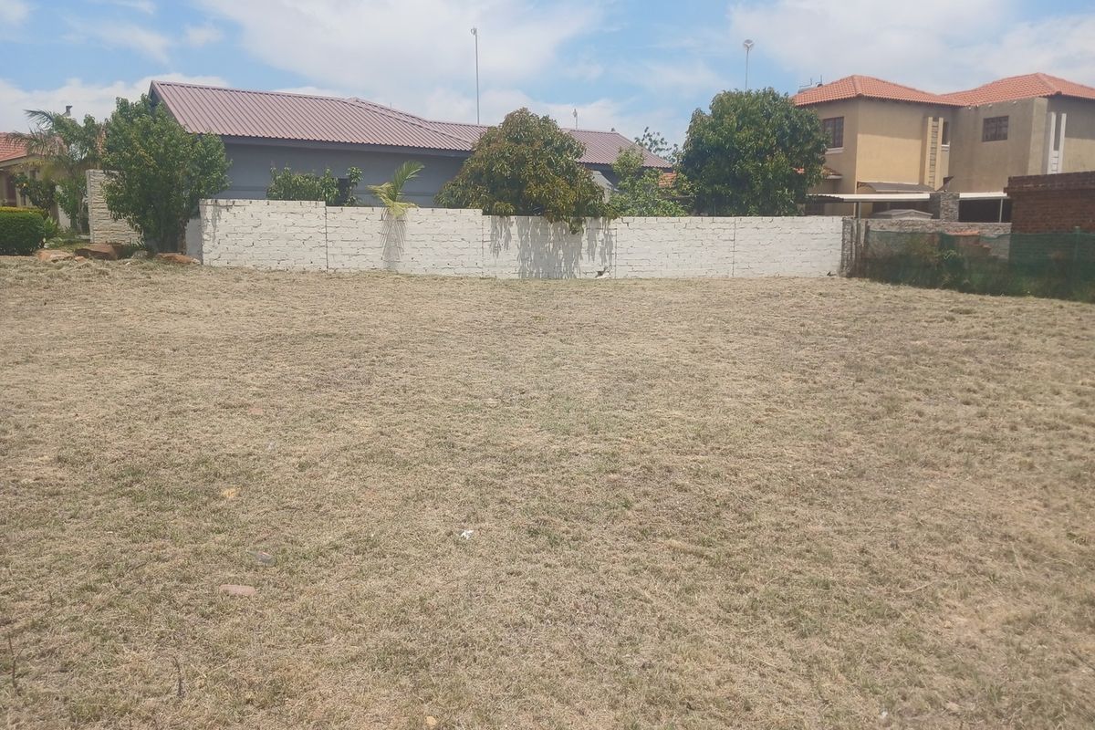 A vacant residential plot featuring a level grass lawn and a perimeter boundary wall, situated in a developed neighborhood.
