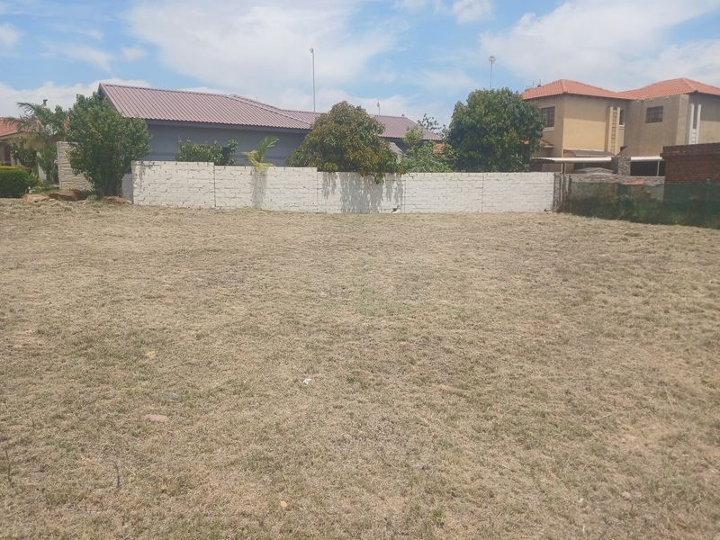 A vacant residential plot featuring a level grass lawn and a perimeter boundary wall, situated in a developed neighborhood.