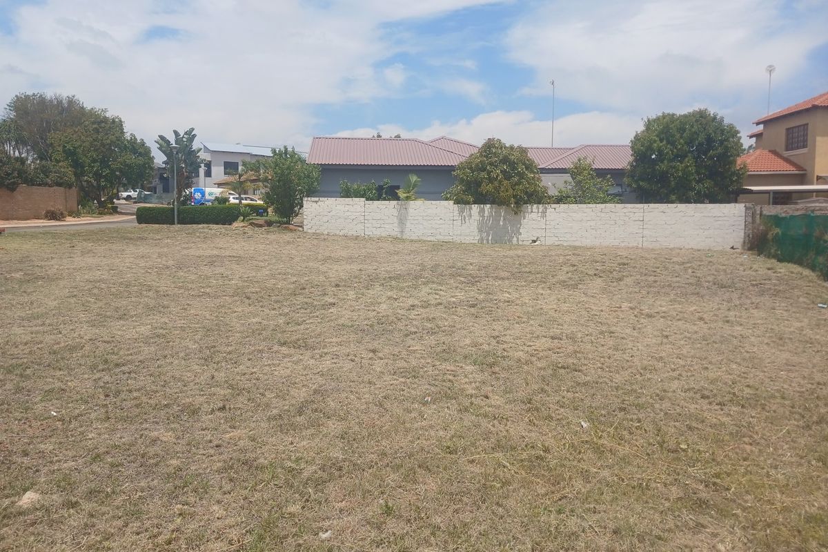 A vacant residential plot featuring a level grass lawn and a perimeter boundary wall, situated in a developed neighborhood.