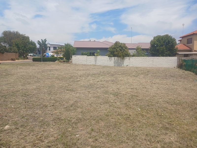 A vacant residential plot featuring a level grass lawn and a perimeter boundary wall, situated in a developed neighborhood.