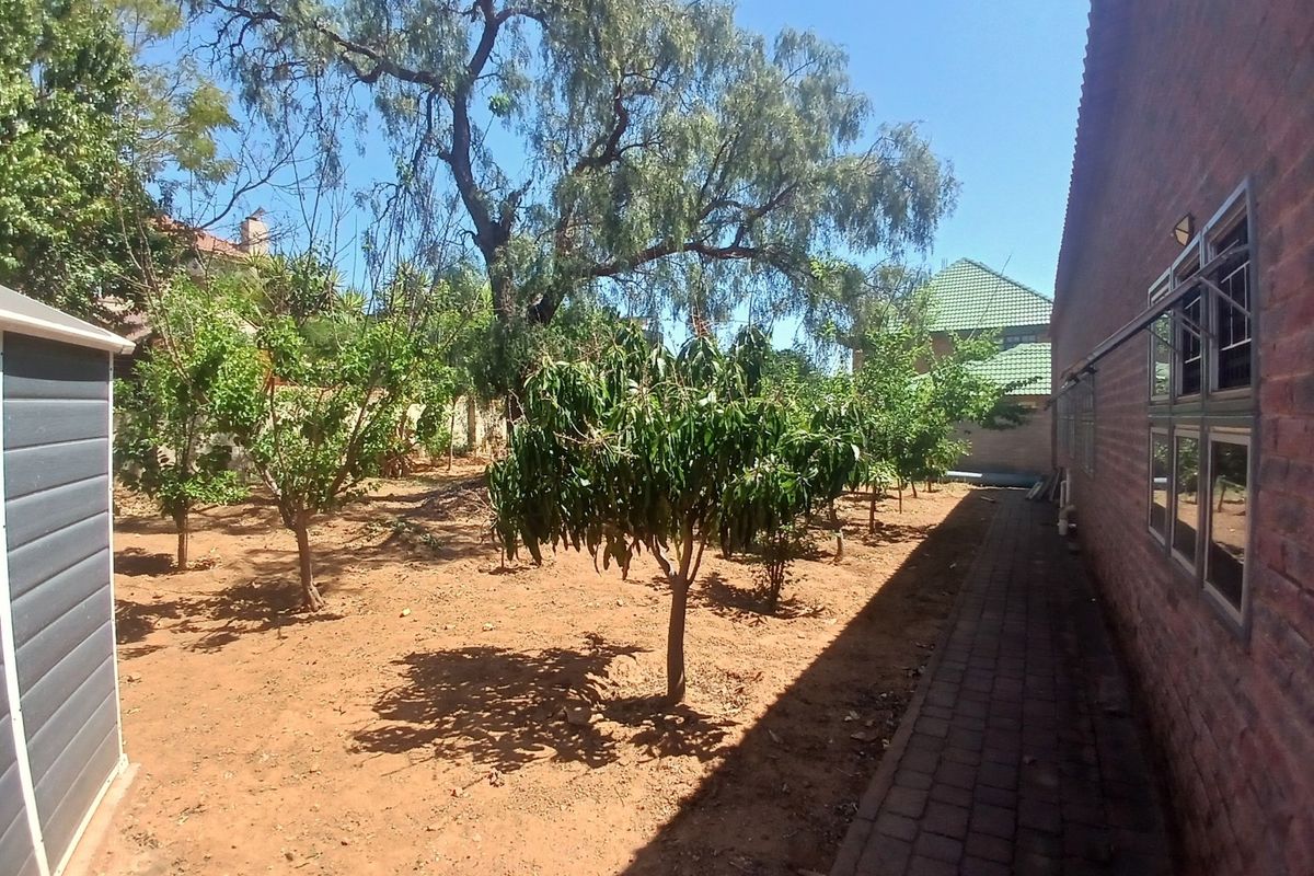 A rear garden area featuring a paved walkway alongside the brick exterior wall, mature trees, and a storage shed.