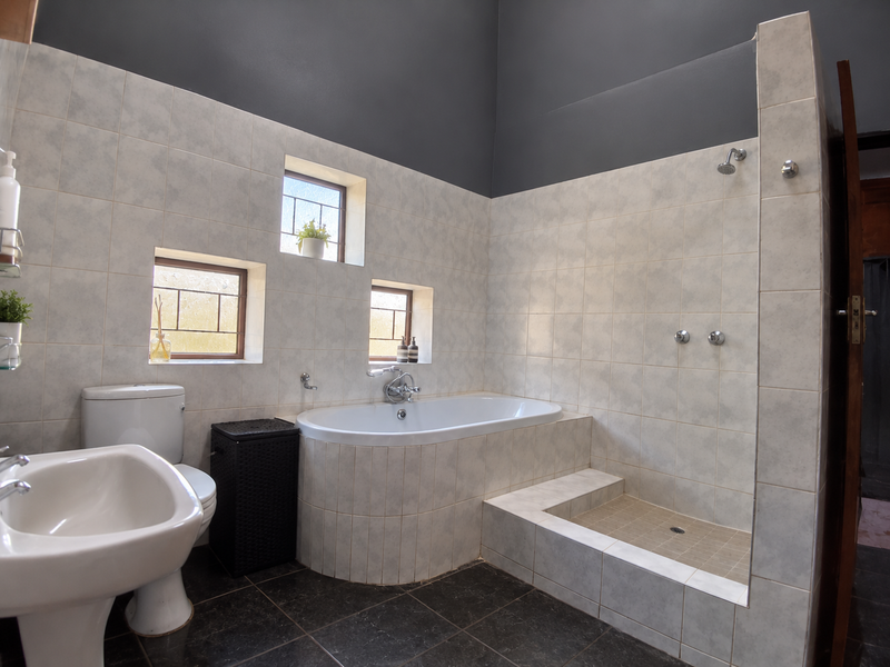 A functional bathroom featuring a built-in bathtub, a walk-in shower with tiled base, and a pedestal basin, finished with neutral wall tiles.