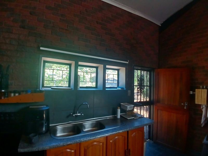 Kitchen area featuring exposed brick walls, wooden cabinetry, laminate countertops, and a double bowl stainless steel sink with a mixer tap.