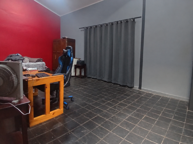 A bedroom featuring dark tiled flooring, a bold red accent wall, and grey wall finishes with a curtained window.