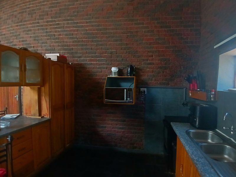 A kitchen featuring exposed brick walls, wooden cabinetry, and a double stainless steel sink with laminate countertops.