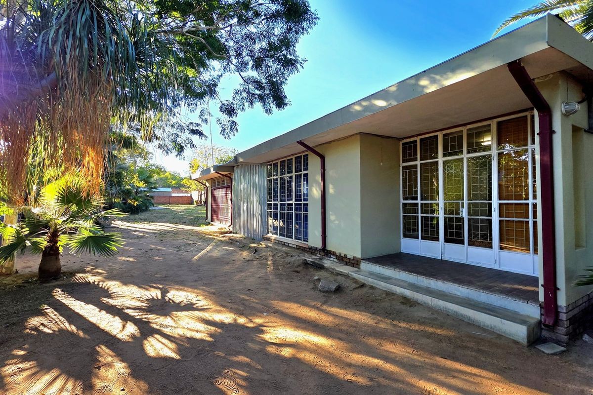 Rear view of the office building featuring a concrete patio, metal-framed glass doors with security grilles, and surrounding garden area.