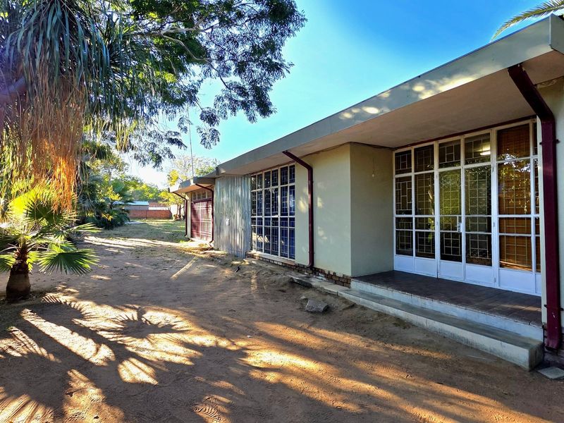 Rear view of the office building featuring a concrete patio, metal-framed glass doors with security grilles, and surrounding garden area.