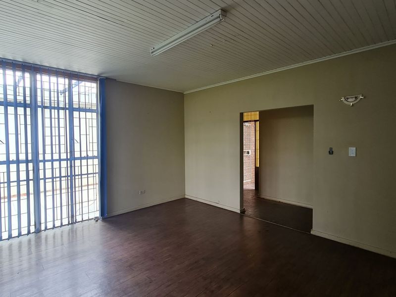 An empty office space featuring laminate flooring, a timber ceiling, and large windows fitted with security bars.