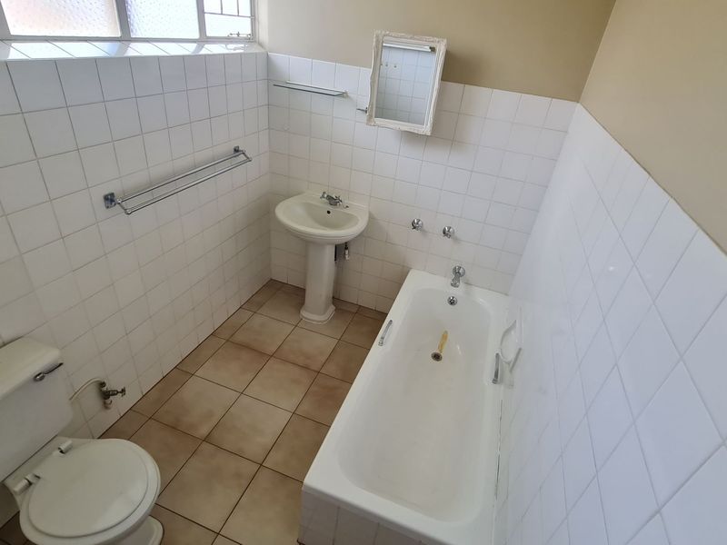 A functional bathroom featuring a pedestal basin, built-in bathtub, and toilet with white wall tiling and neutral floor tiles.