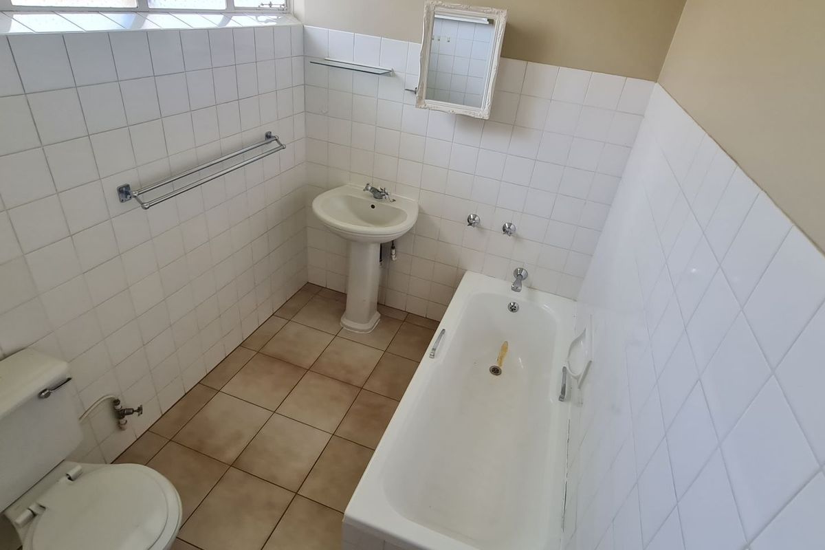 A functional bathroom featuring a pedestal basin, built-in bathtub, and toilet with white wall tiling and neutral floor tiles.