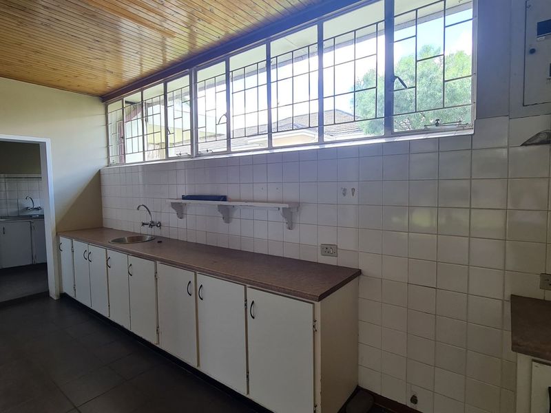 A functional kitchen area featuring built-in cabinetry, a stainless steel sink, tiled backsplash, and timber ceiling, offering a blank canvas for renovation.