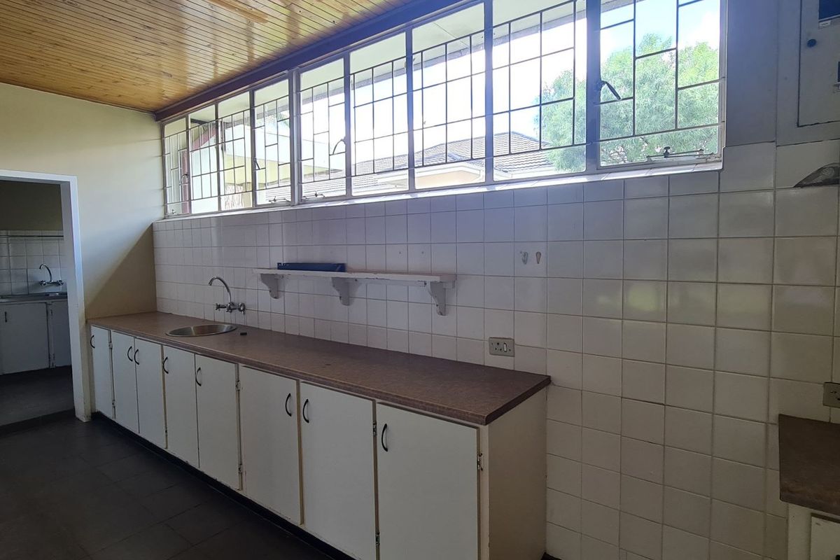 A functional kitchen area featuring built-in cabinetry, a stainless steel sink, tiled backsplash, and timber ceiling, offering a blank canvas for renovation.