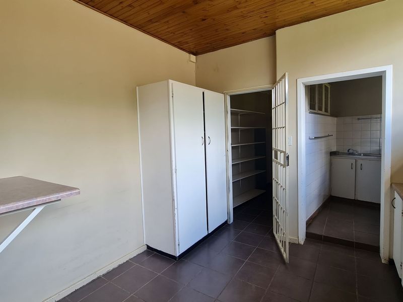A functional scullery area featuring tiled flooring, built-in storage cupboards, and an adjacent pantry space with shelving and a sink.