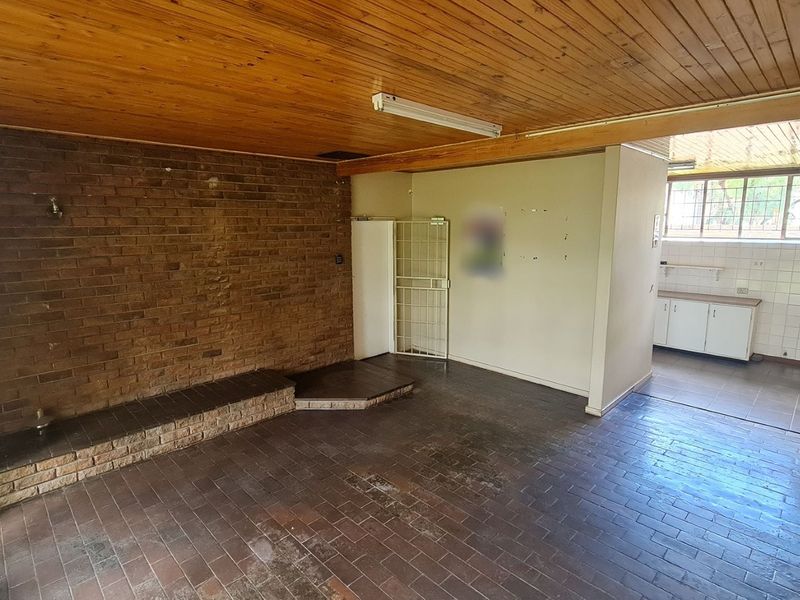 Open plan office space featuring exposed brickwork, timber ceiling, and tiled flooring, with an adjacent kitchenette area and security gate access.