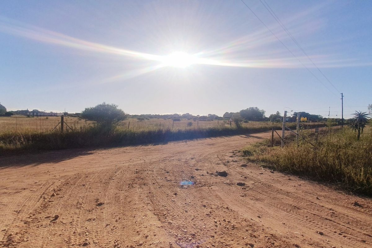 A view of a dirt road leading towards a vacant residential plot with existing wire fencing and utility infrastructure.