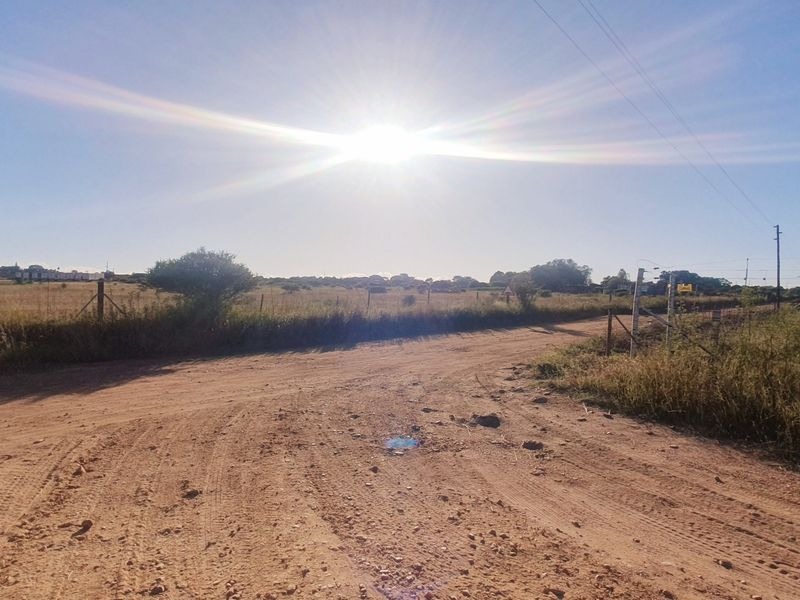A view of a dirt road leading towards a vacant residential plot with existing wire fencing and utility infrastructure.