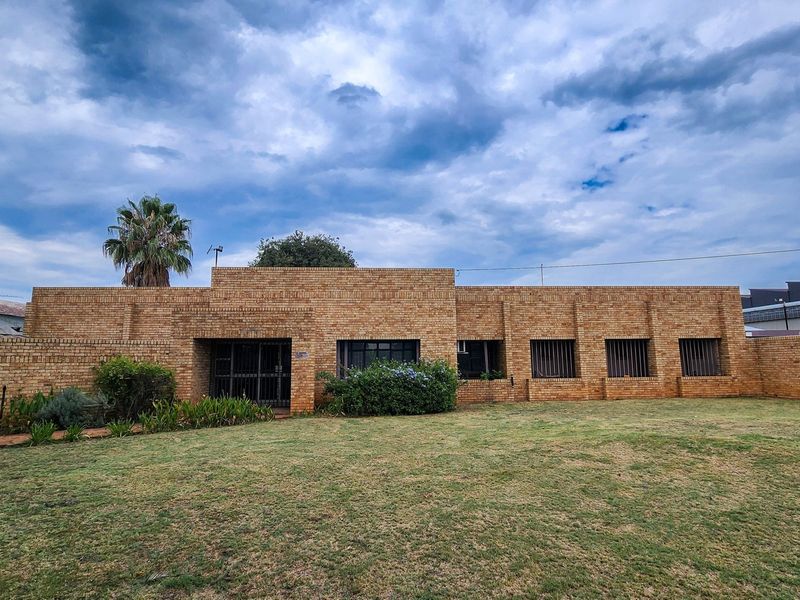 A single-story commercial building featuring a face brick facade, security bars on windows, and a gated entrance set within a grassed area.