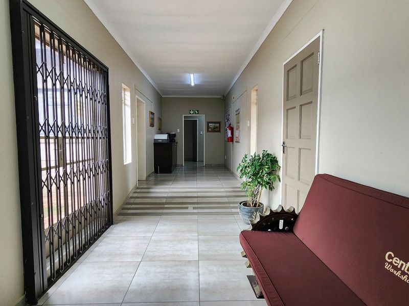 A well-lit commercial hallway featuring tiled flooring, a security gate, and access to multiple office or workshop spaces.