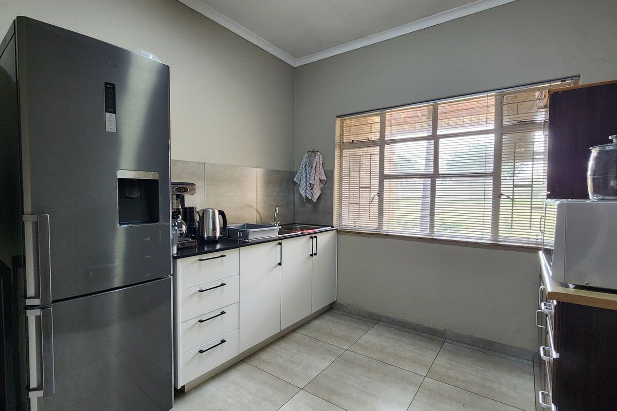 A functional kitchen featuring modern white cabinetry, stone countertops, a stainless steel sink, and large windows with venetian blinds.