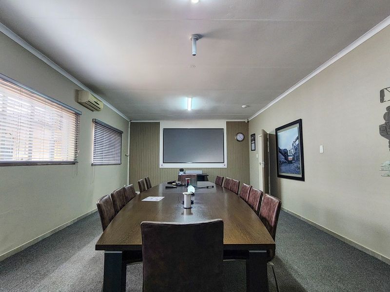 A professional boardroom or meeting room featuring carpeted flooring, venetian blinds, an integrated projector screen, and wall-mounted air conditioning.
