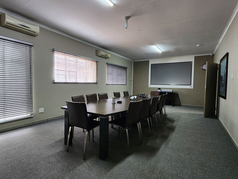 A functional commercial boardroom featuring carpeted flooring, split-system air conditioning, venetian blinds, and a wall-mounted projector screen.