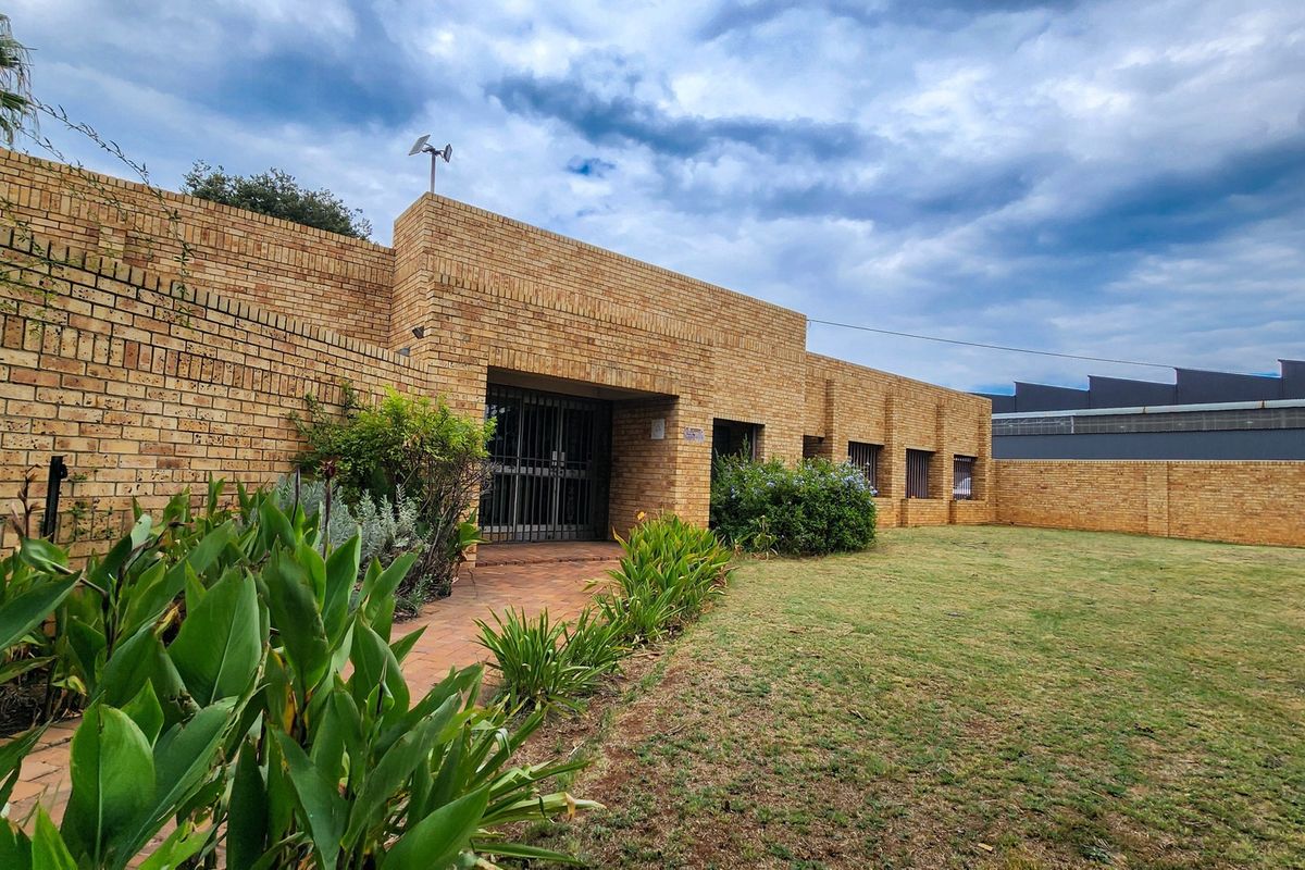 A well-maintained commercial property exterior featuring a face brick facade, secure entrance gate, paved walkway, and a spacious lawn area.