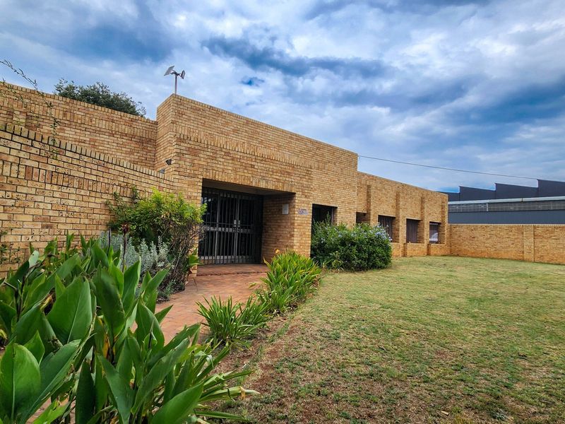 A well-maintained commercial property exterior featuring a face brick facade, secure entrance gate, paved walkway, and a spacious lawn area.