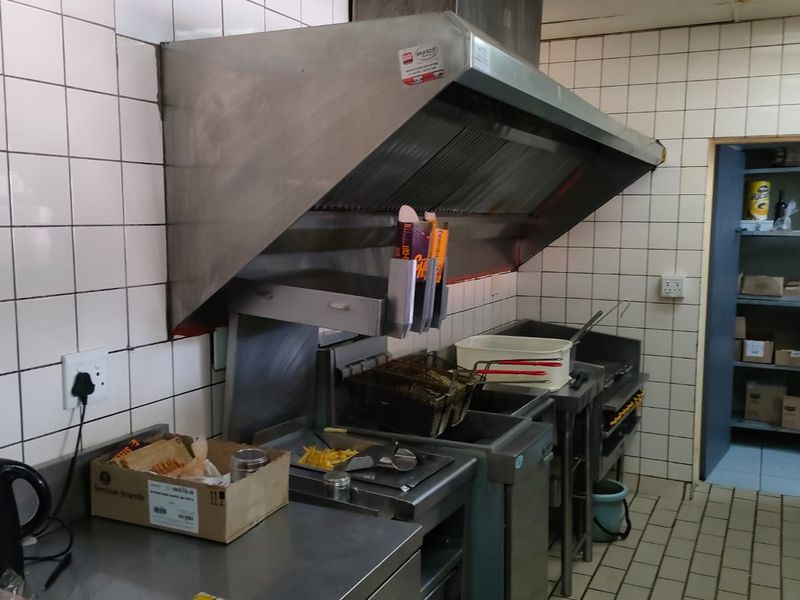 Commercial kitchen area featuring a stainless steel extractor hood, deep fryer station, tiled wall finishes, and a dedicated storage pantry.