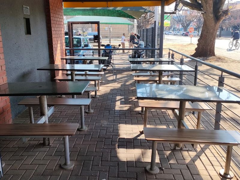 A covered outdoor patio area featuring brick wall accents, paved flooring, and metal safety railings, suitable for office break-out or seating space.