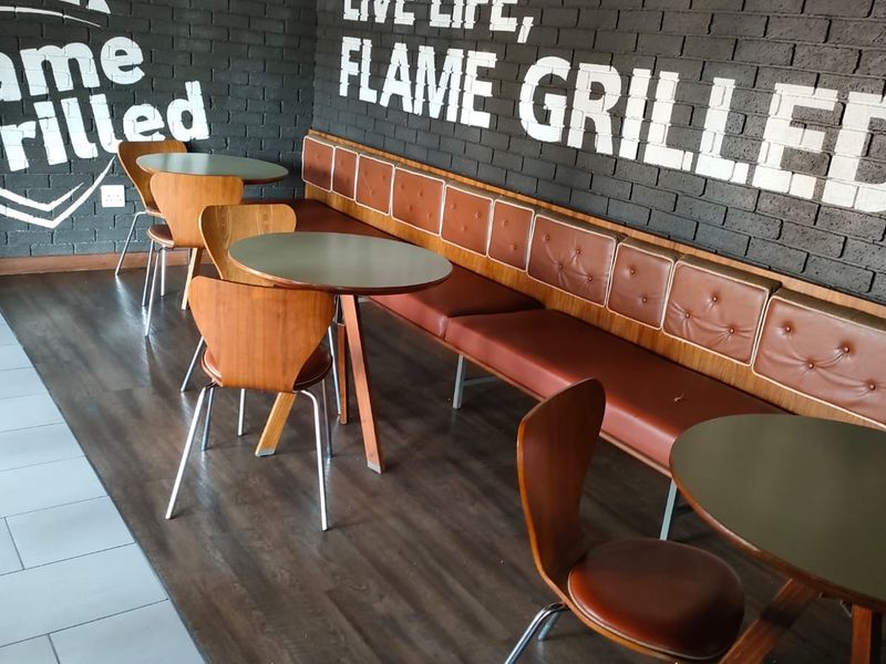 A commercial office or dining space featuring dark exposed brick walls with branding, built-in leather bench seating, and wood-look laminate flooring.