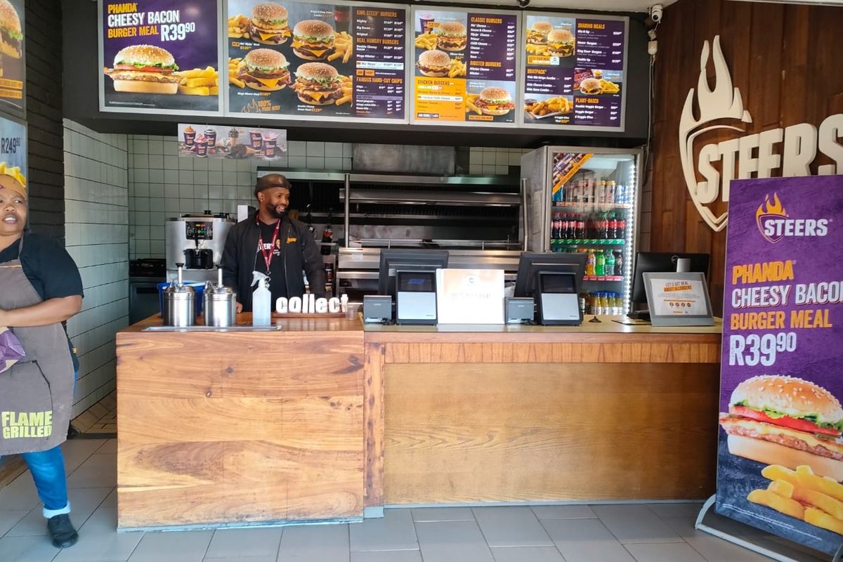 A commercial kitchen service area featuring a wooden service counter, tiled flooring, and integrated commercial food preparation and refrigeration equipment.