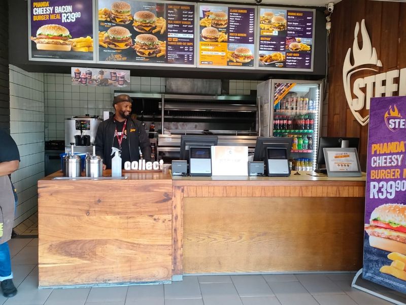 A commercial kitchen service area featuring a wooden service counter, tiled flooring, and integrated commercial food preparation and refrigeration equipment.