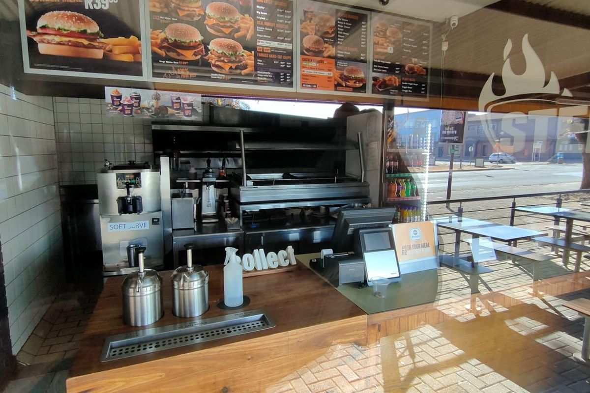 A commercial kitchen service area featuring a built-in grill, extractor system, soft serve machine, and a wooden service counter for customer orders.