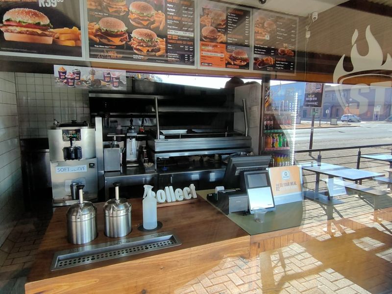 A commercial kitchen service area featuring a built-in grill, extractor system, soft serve machine, and a wooden service counter for customer orders.