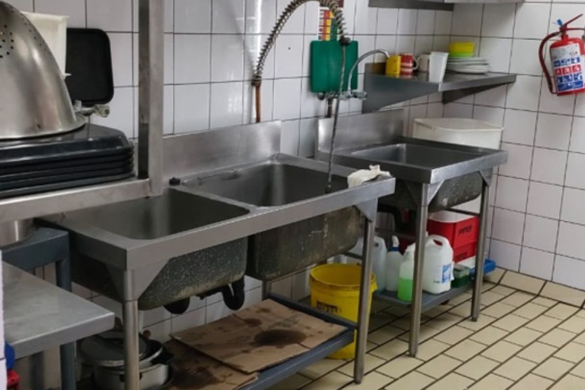 Commercial scullery area featuring stainless steel sinks, tiled wall finishes, and industrial floor drainage, suitable for high-volume food preparation or wash-up tasks.