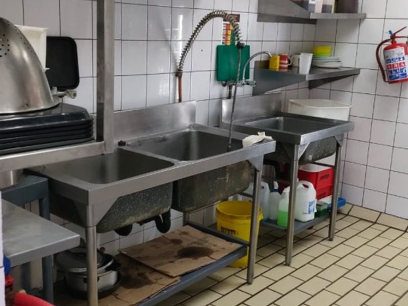 Commercial scullery area featuring stainless steel sinks, tiled wall finishes, and industrial floor drainage, suitable for high-volume food preparation or wash-up tasks.