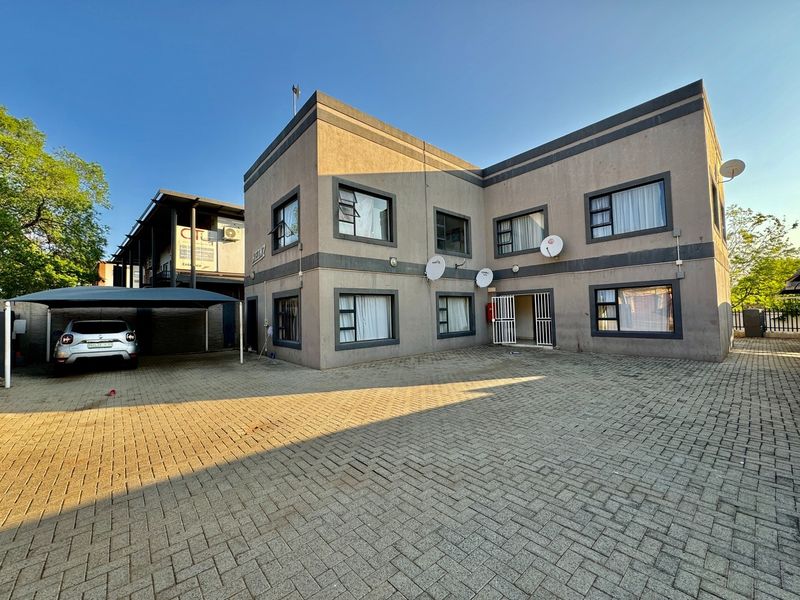 Exterior view of a multi-story apartment building featuring a paved driveway, covered carport, and security gate access.