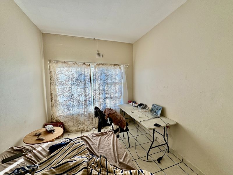 A bedroom featuring tiled flooring and a ventilation grille, requiring cosmetic updates to the wall finishes and flooring to improve its overall appeal.