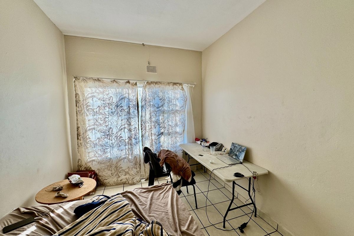 A bedroom featuring tiled flooring and a ventilation grille, requiring cosmetic updates to the wall finishes and flooring to improve its overall appeal.